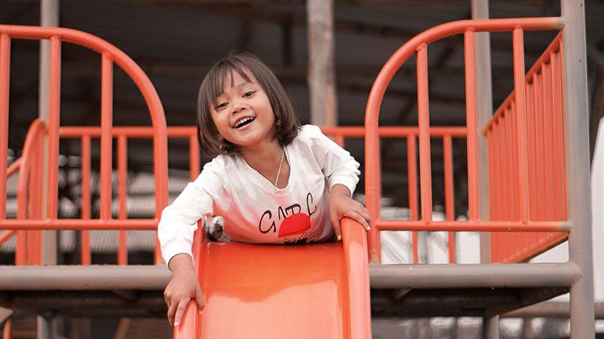 A happy child enjoying playtime on a vibrant orange slide at an outdoor playground