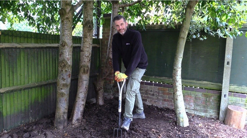 A Red Kite member of staff with a garden fork digging beneath some trees