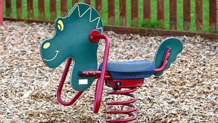 A colorful dinosaur-themed spring rider in an outdoor playground with wood chips