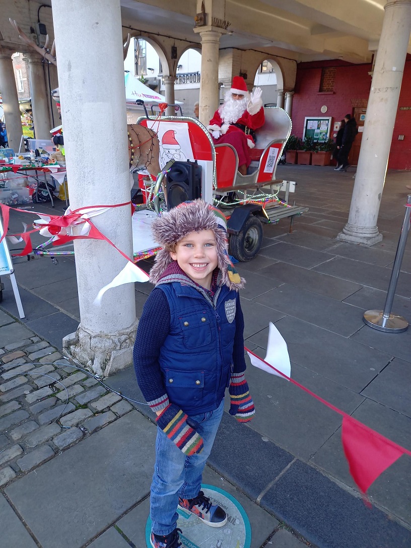 A young child posing in front of Santa in his sleigh
