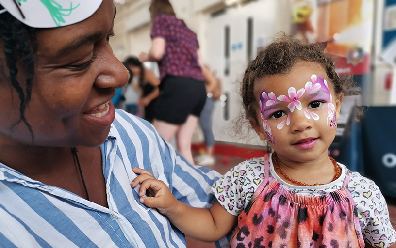 A lady holding a young toddler with her face painted