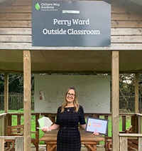 A lady standing by a wooden structure with her medal and certificate