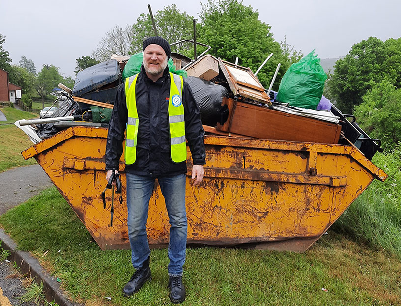 A Red Kite member of staff in a high-vis vest in front of a skip full of waste