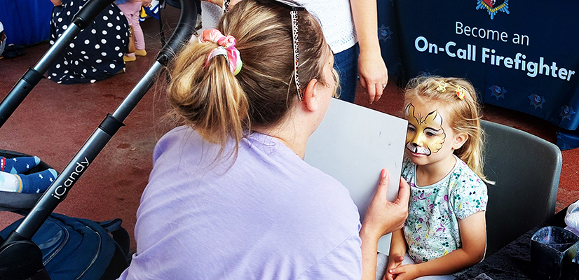 A woman holding a mirror so a child can see her painted face