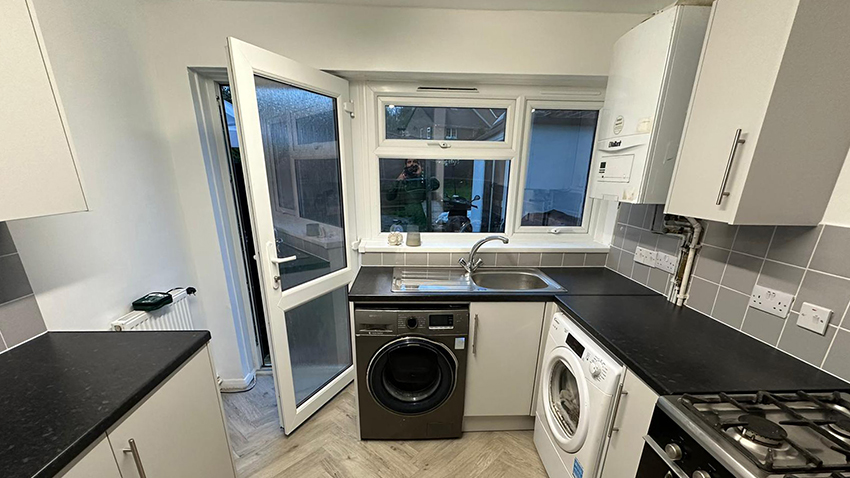 A photo showing a newly-refurbished kitchen; laminate flooring has been laid, granite-effect laminate worktops fitted, and new white vinyl windows and a glazed back door installed